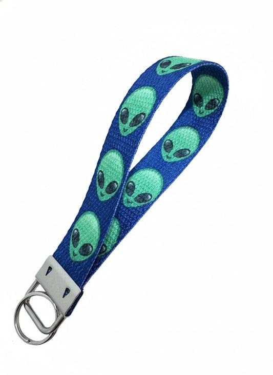 A dark blue fabric wristlet keychain patterned with green alien heads, featuring a silver-toned metal key ring attachment.