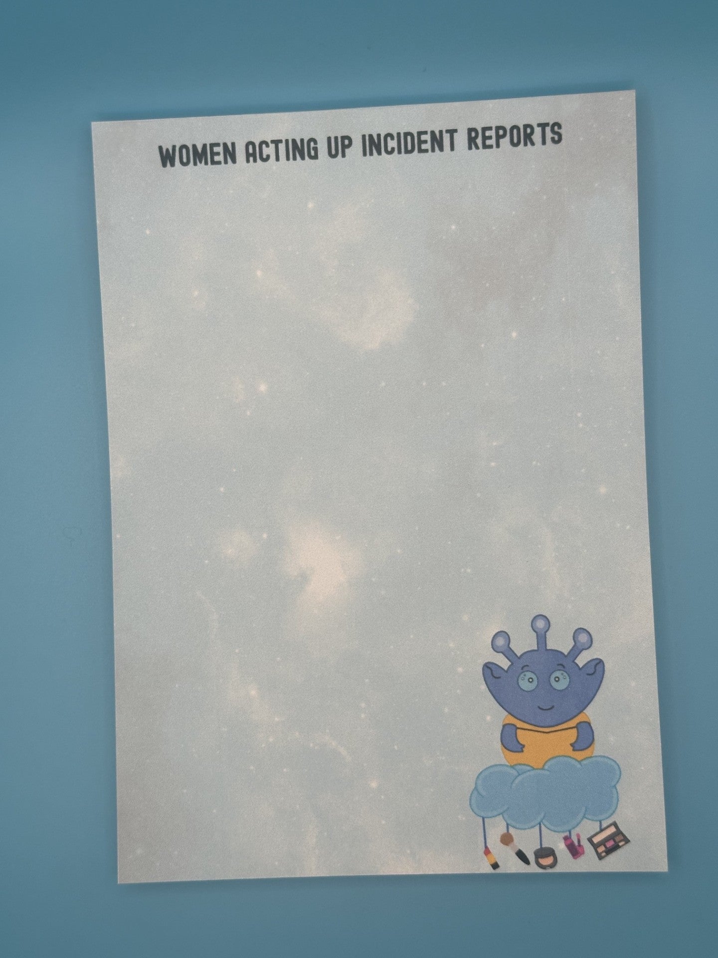 Notepad with character Cosmo Menace that looks like a blue alien floating on a cloud with makeup hanging from it. The notepad has a light blue sparkle background and has a heading on the notepad that states "women acting up incident reports". The notepad is sitting on top of a blue background.