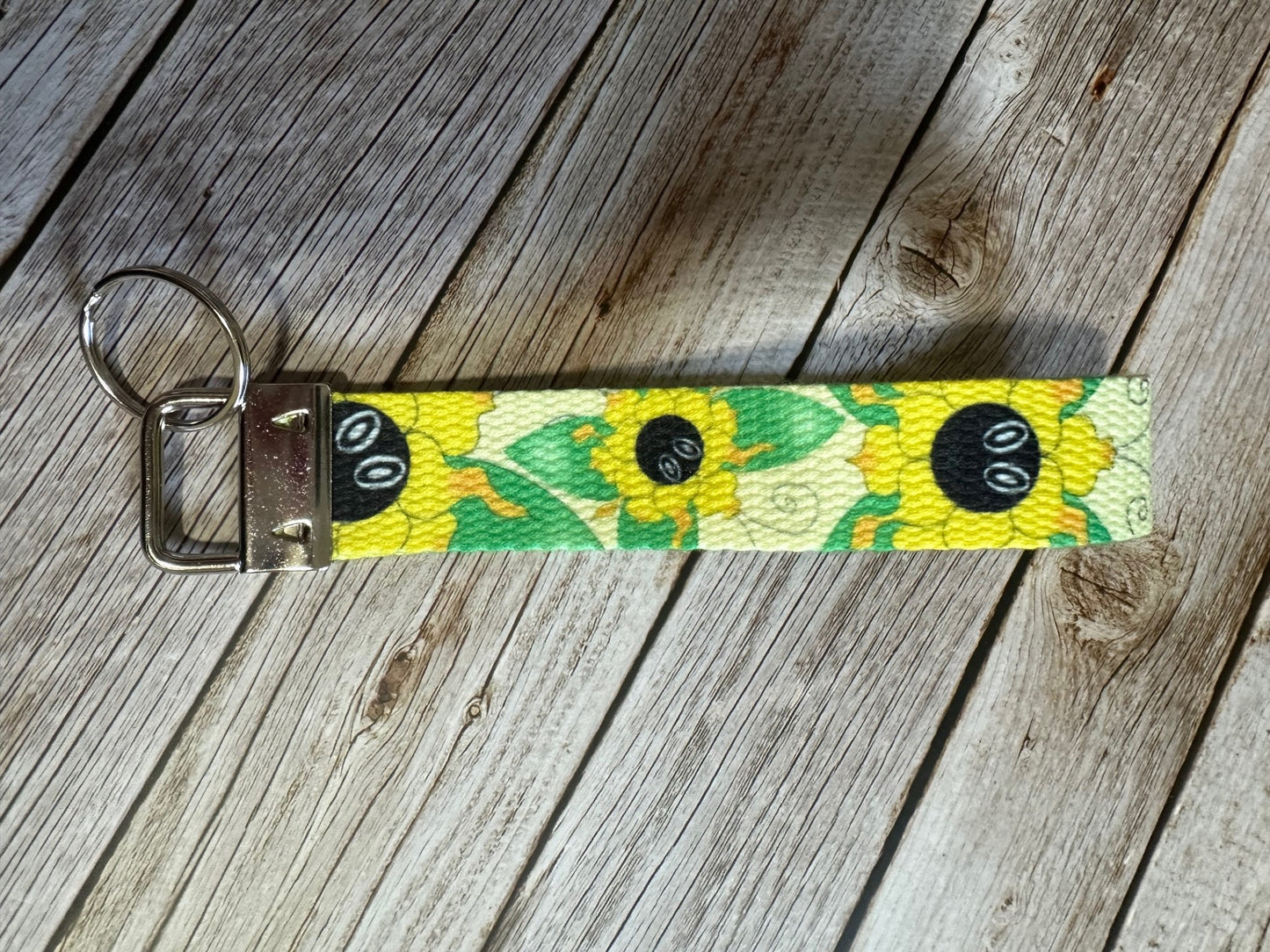 Keychain wristlet with a yellow flower that also has green shape butterfly wings coming from it. The wristlet is sitting on a wooden surface.