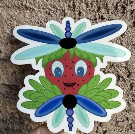 Sticker of a strawberry with dragonfly wings that is blue and light turquoise in color. The character has green leaves coming out of it. The sticker background is a textured wall.