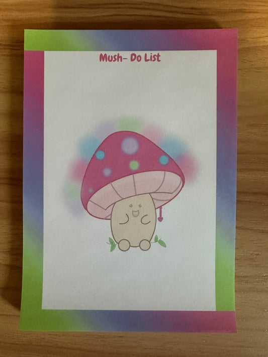 Notepad with heading "mush do list" with a cartoon mushroom design on a wooden surface.