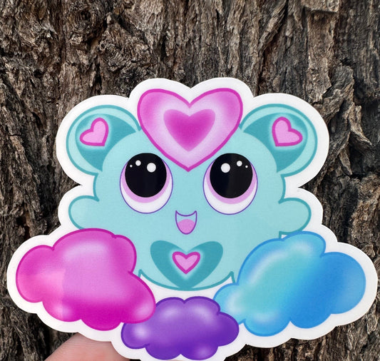 A fictional Cartoon character with heart-shaped ears that has different colors. The colors on the character are blue, pink, and purple pastel. The character is on a colorful pastel of the same color, and the background is a tree branch.
