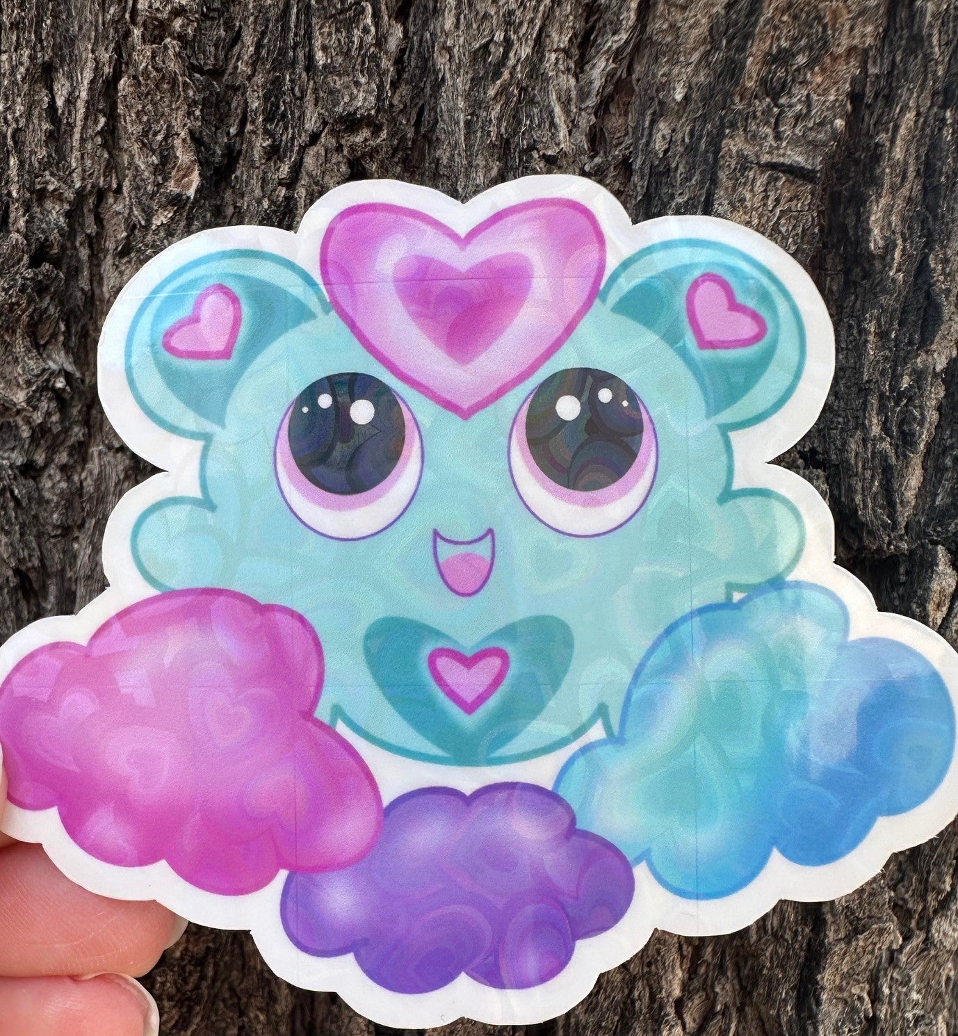 A fictional Cartoon character with heart-shaped ears that has different colors. The colors on the character are blue, pink, and purple pastel. The character is on a colorful pastel of the same color, and the background is a tree branch.