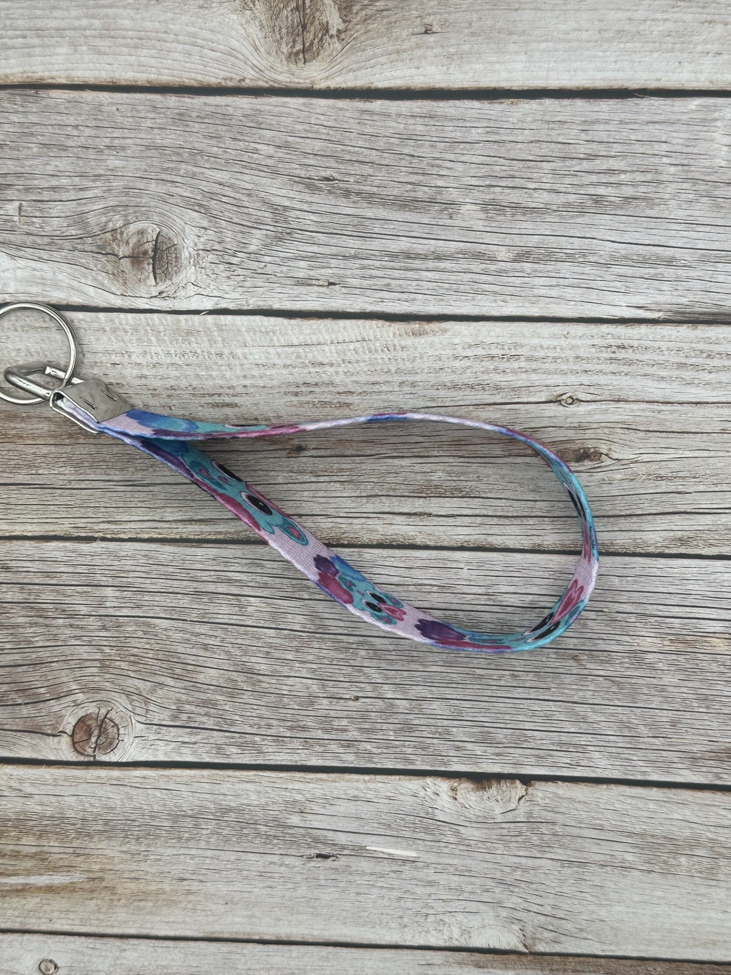 Unique fictional character that is blue and has pink and turquoise hearts on it. The character is also on a purple, pink and blue cloud and has black eyes with pink in them. The background color of the wristlet is light pink. The wristlet is sitting on top of a wooden background.