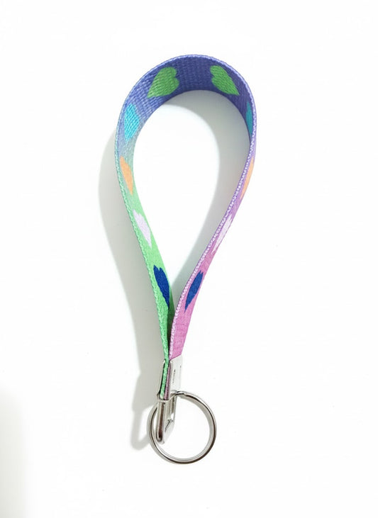 A purple fabric wristlet keychain featuring a vertical pattern of turquoise, orange, white, and dark blue hearts.