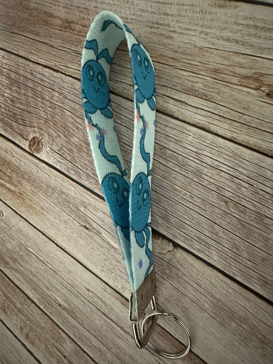 Side view of the keychain wristlet with a blue-colored fictional cartoon character on a wooden surface.