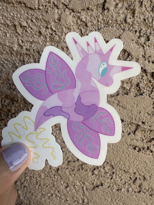 Fictional character sticker that is light purple and dark purple, that looks like a dragon and also has wings with turquoise lines. The character has five horns coming from its head that are pink and purple, while the tail is yellow and light pink. The character has light blue eyes.