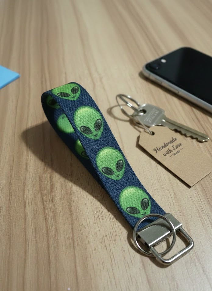 Keychain with alien pattern on a wooden surface next to a phone and key