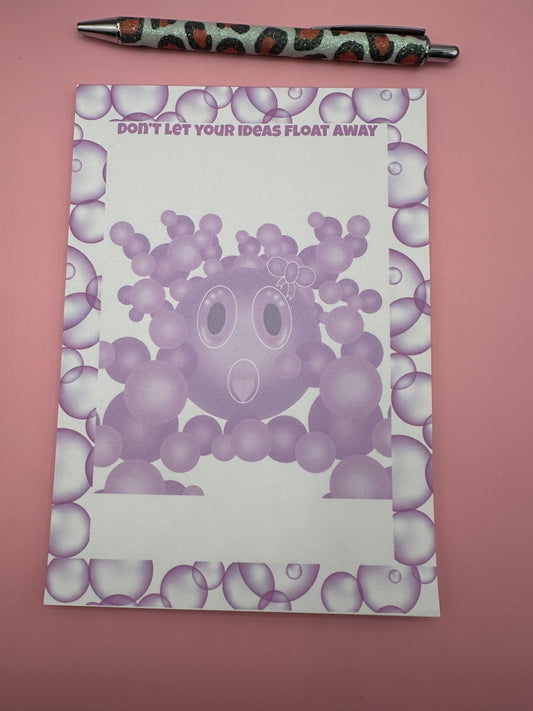 A notepad with bubble character that is purple with a white bow on head and a heart shape mouth surrounded by other size bubbles. The notepad is outlined with purple bubbles and has a heading of "Don't let your ideas float away". The notepad is sitting on a pink background with a pen.