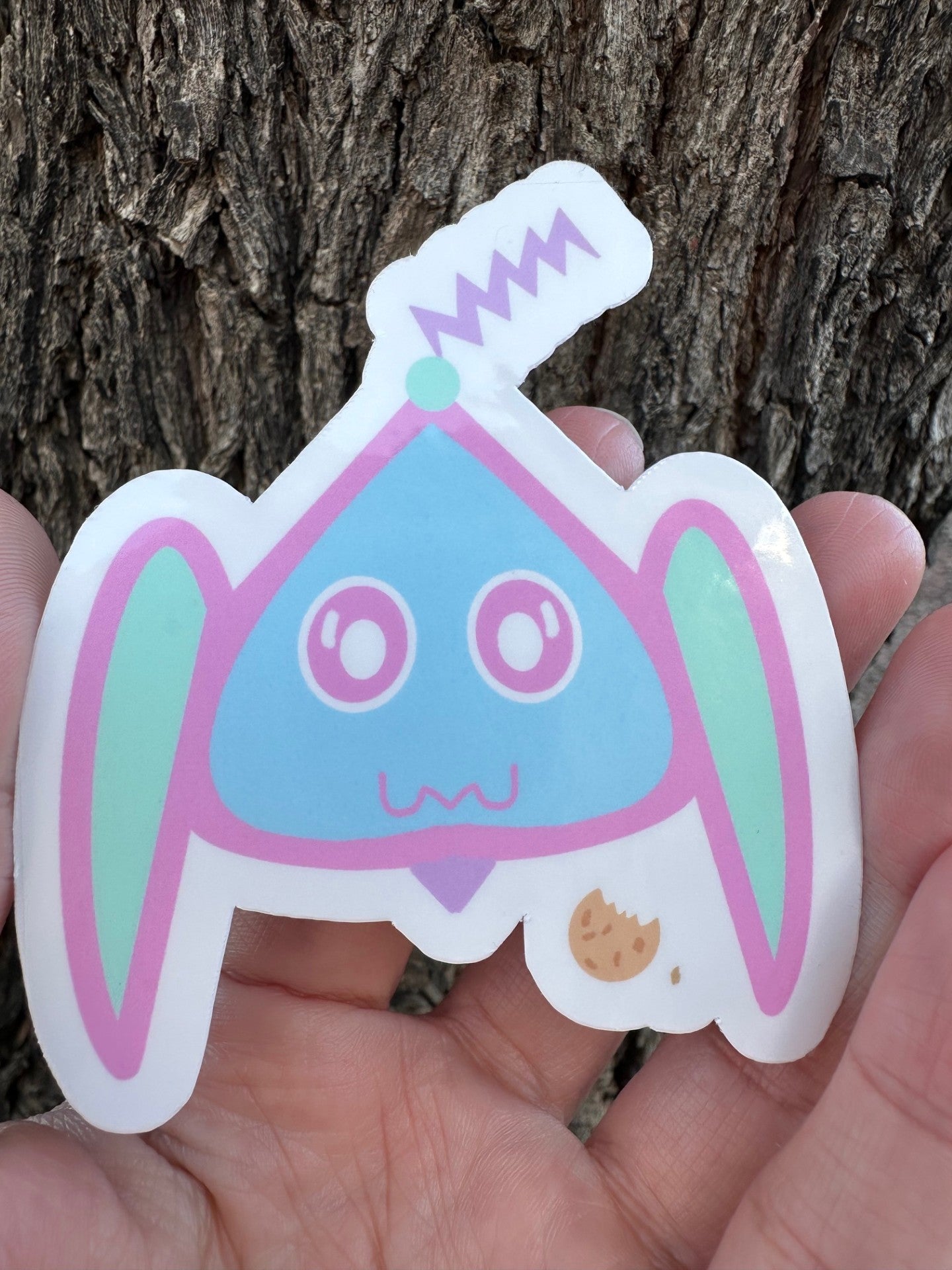 Cartoon sticker from space held in front of a tree trunk.