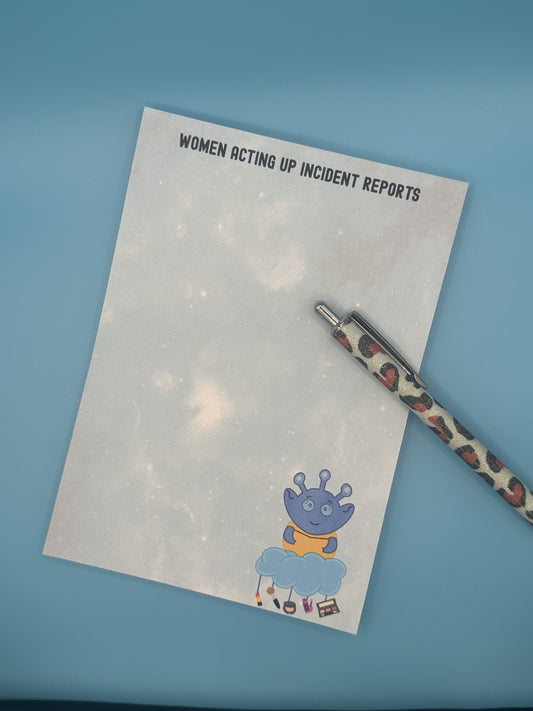 Notepad with character Cosmo Menace that looks like a blue alien floating on a cloud with makeup hanging from it. The notepad is a light blue sparkle background and has a heading on notepad that states "women acting up incident reports". The notepad is sitting on top of a blue background and a pen.