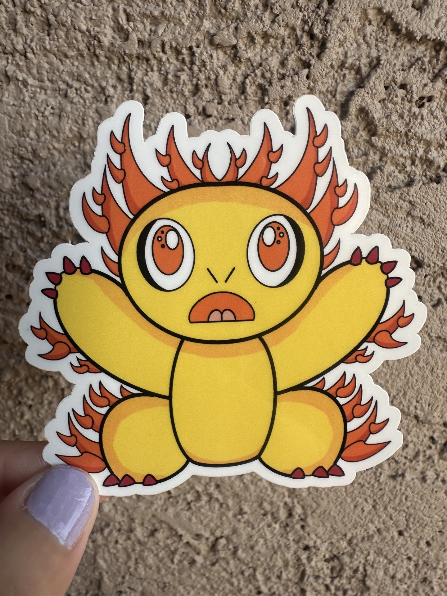 Fictional character sticker that is yellow and has multiple spikes coming out of the character that are orange. The character has red nails with big orange eyes with white and black in them.  