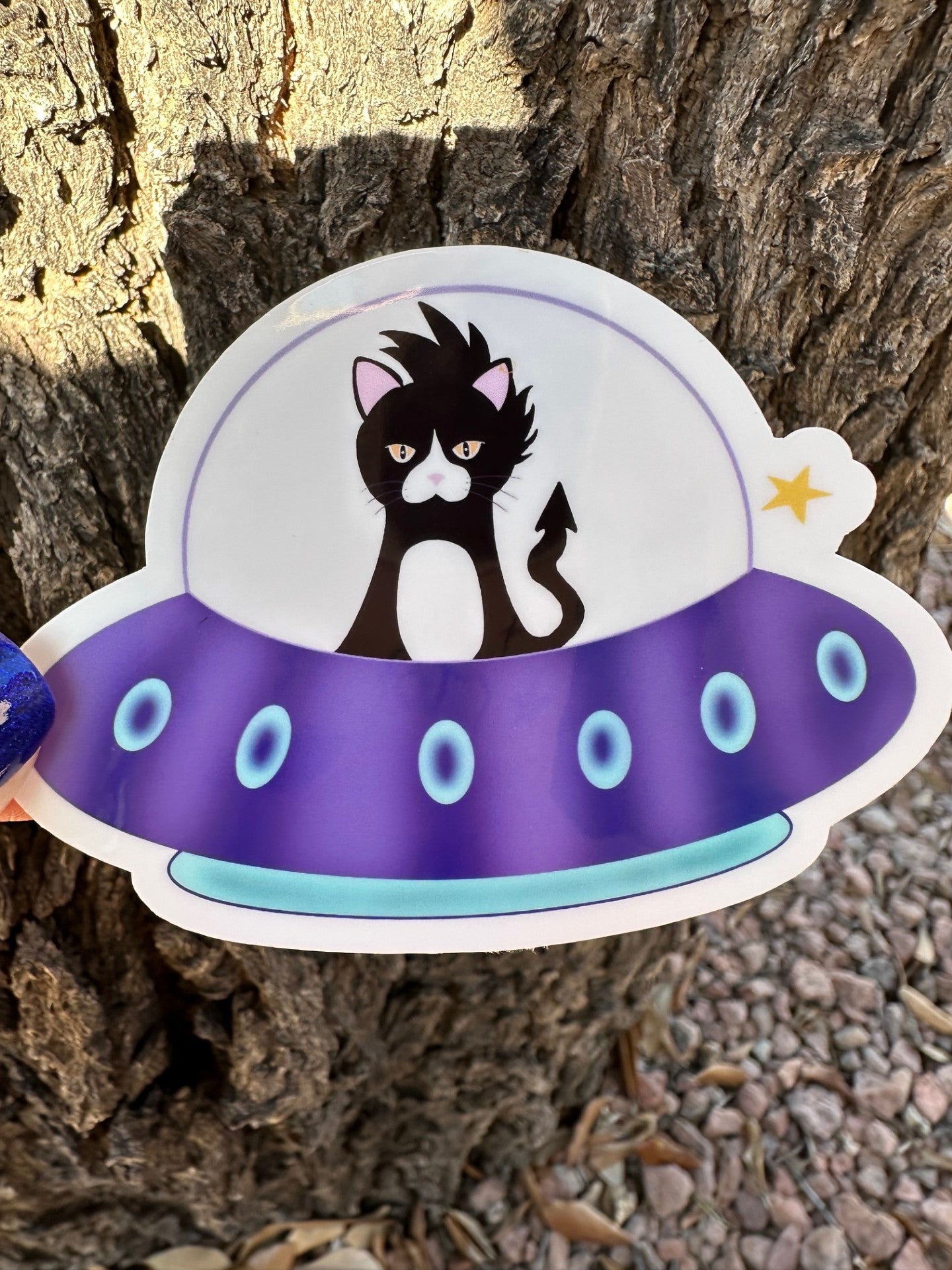 Sticker of a cat in a UFO against a tree bark background.