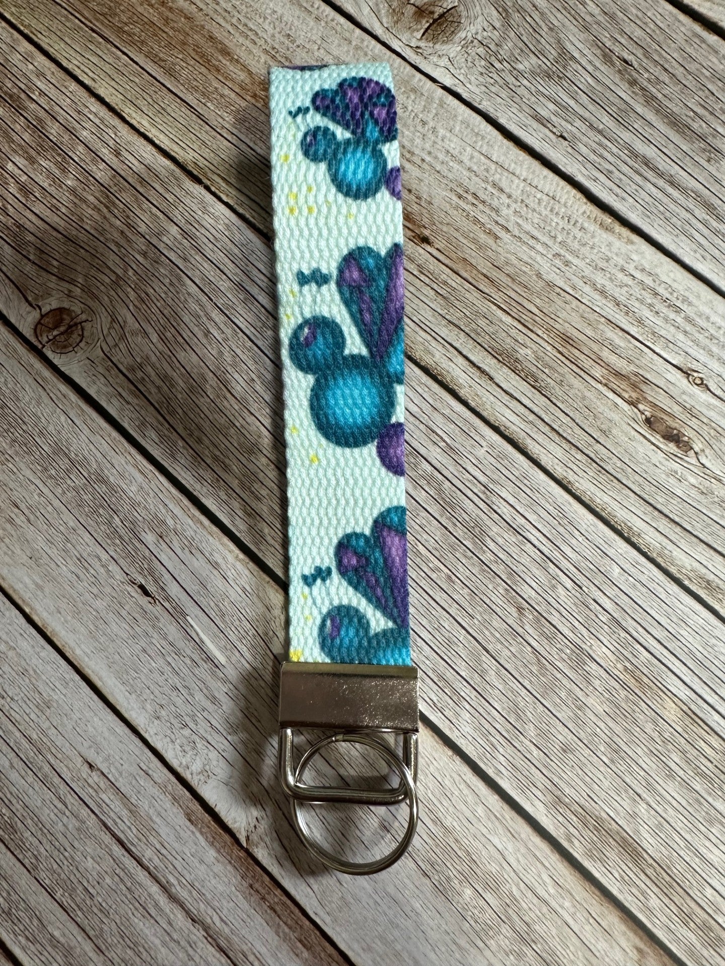 Keychain back view of the wristlet with fictional character love mist that is dark blue and purple sitting on a wooden surface.
