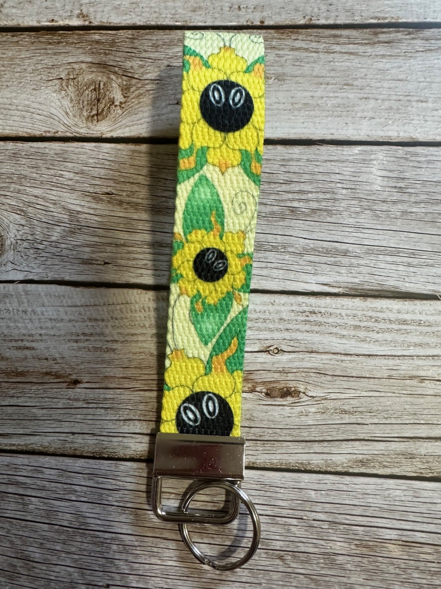 Wristlet keychain with sunflower design that also has butterfly wings coming from it. The wrislet is sitting on a wooden surface. 