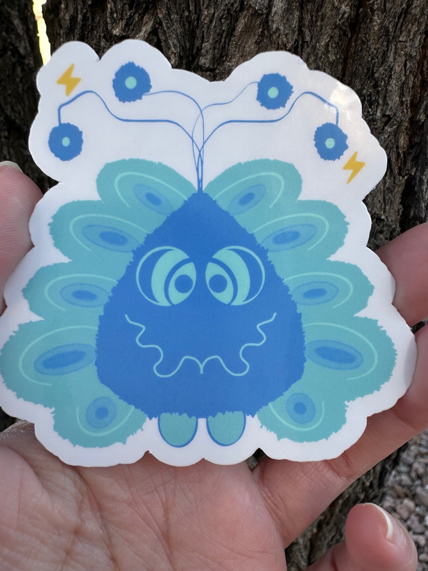 A sticker featuring a friendly blue character with a wavy smile, antenna with spheres, peacock-like feather details, and small yellow lightning bolts.