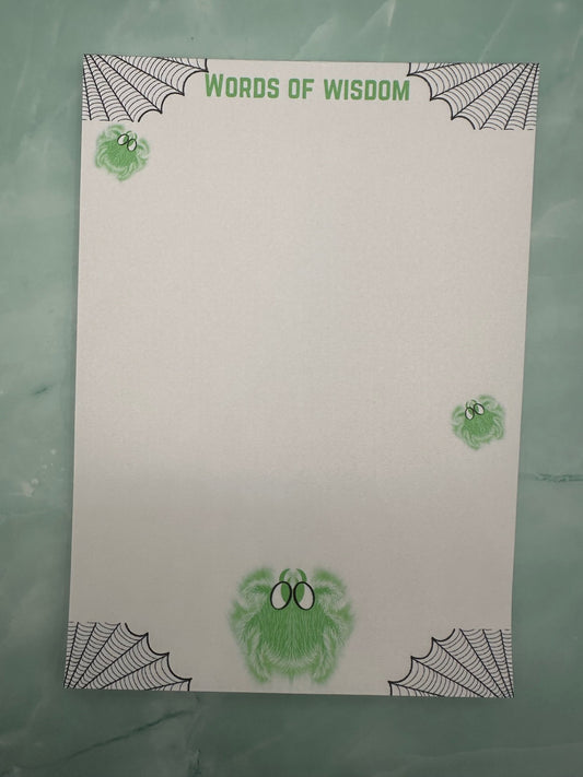 A notepad with green spider character that glows and has white hair with green eyes. Around the four corners of the notepad is spider webs and the heading of the notepad states "Words of wisdom". The notepad is sitting on a light green background. 