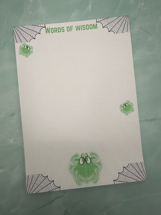 A notepad with green spider character that glows and has white hair with green eyes. Around the four corners of the notepad is spider webs and the heading of the notepad states "Words of wisdom". The notepad is sitting on a light green background. 