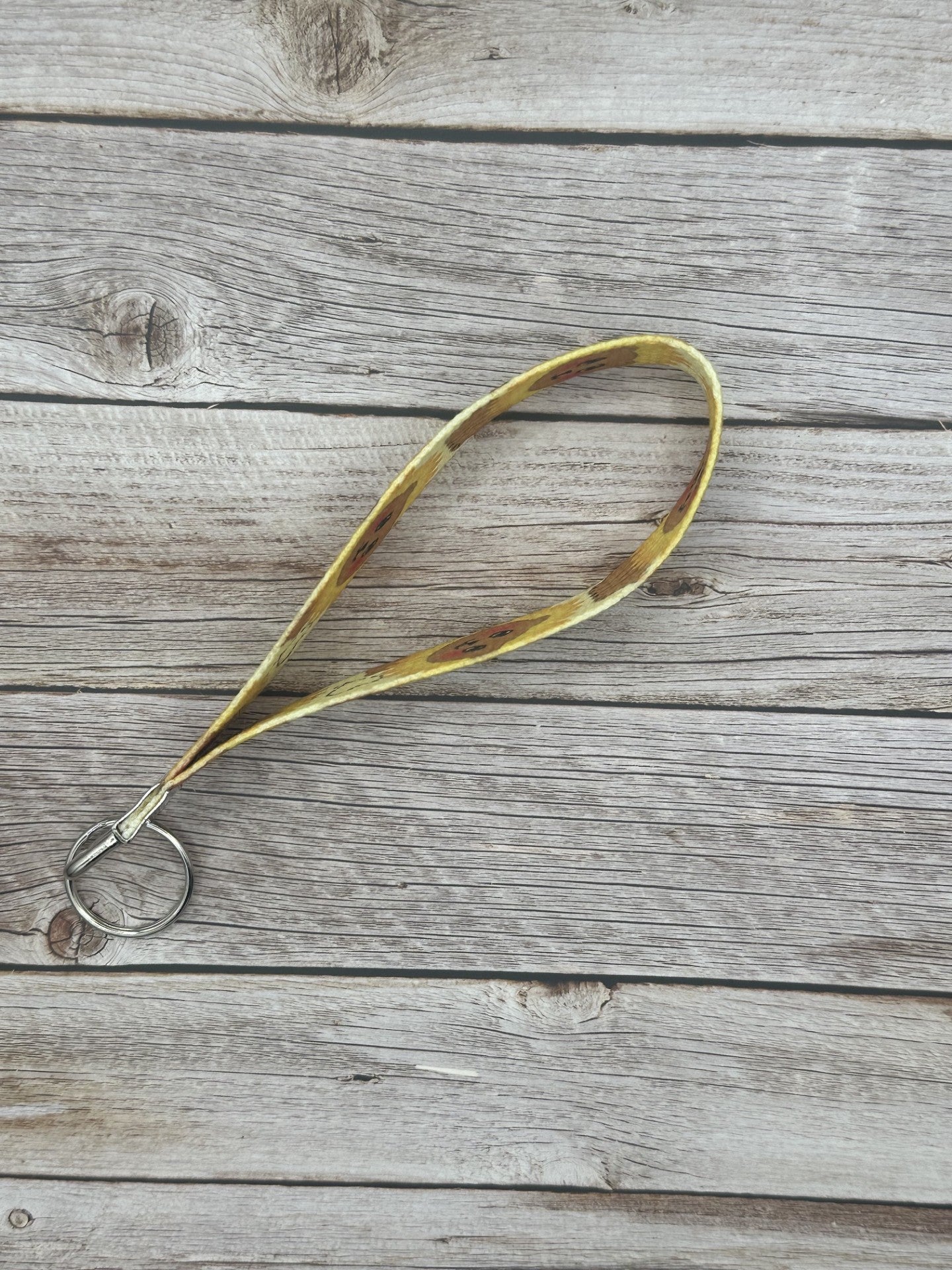 Side view of the wristlet keychain with a brown bear that has black eyes and rosy cheeks. The bear has a sunflower shape around its head, and a heart on the bottom of the wristlet. The keychain is on a wooden surface.