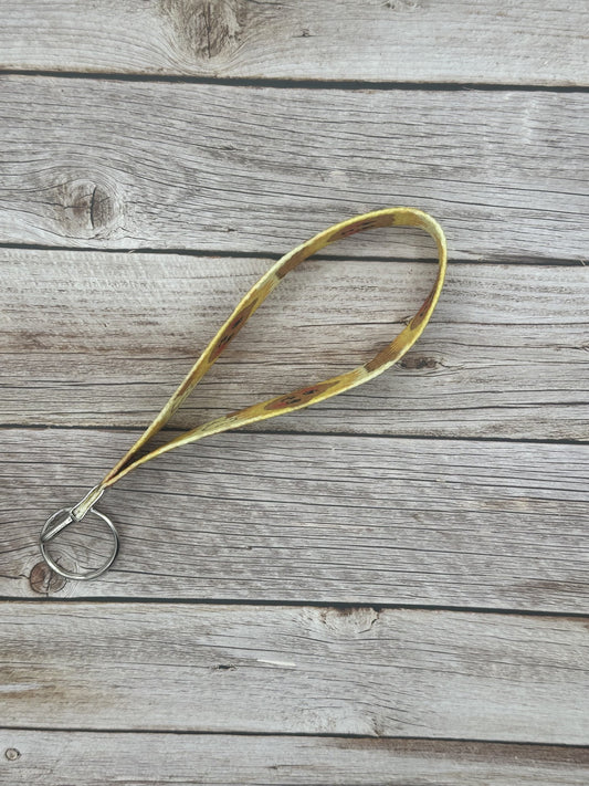 Side view of the wristlet keychain with a brown bear that has black eyes and rosy cheeks. The bear has a sunflower shape around its head, and a heart on the bottom of the wristlet. The keychain is on a wooden surface.