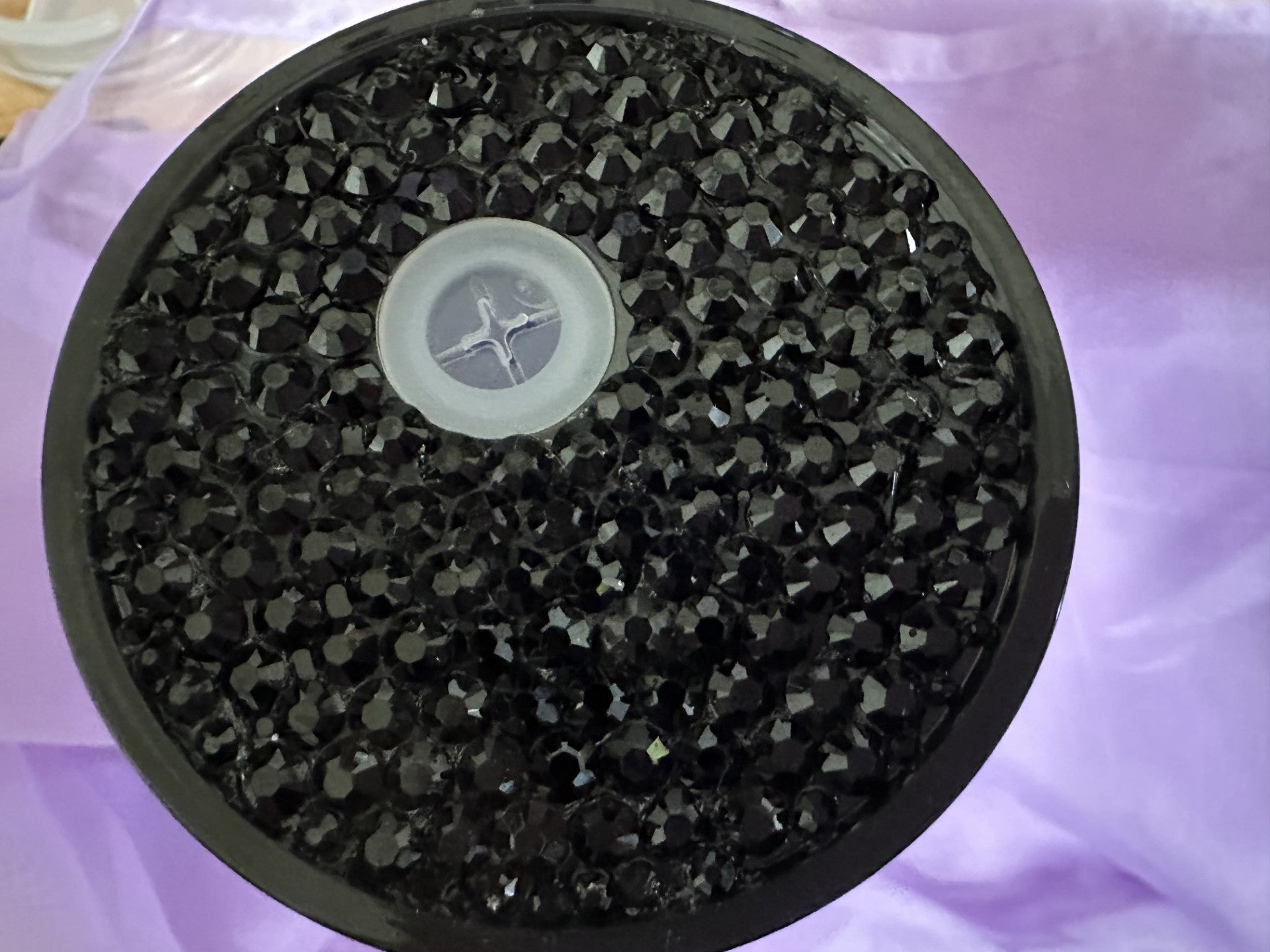Round black filter with central component rhinestones on a purple surface.