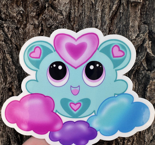 A fictional Cartoon character with heart-shaped ears that has different colors. The colors on the character are blue, pink, and purple pastel. The character is on a colorful pastel of the same color, and the background is a tree branch. 