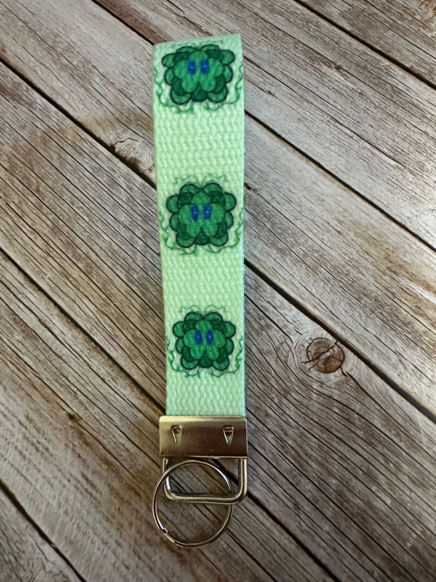 Green keychain strap with green patterns of the character on a wooden. The fictional character, Lucky, with his vines up.
