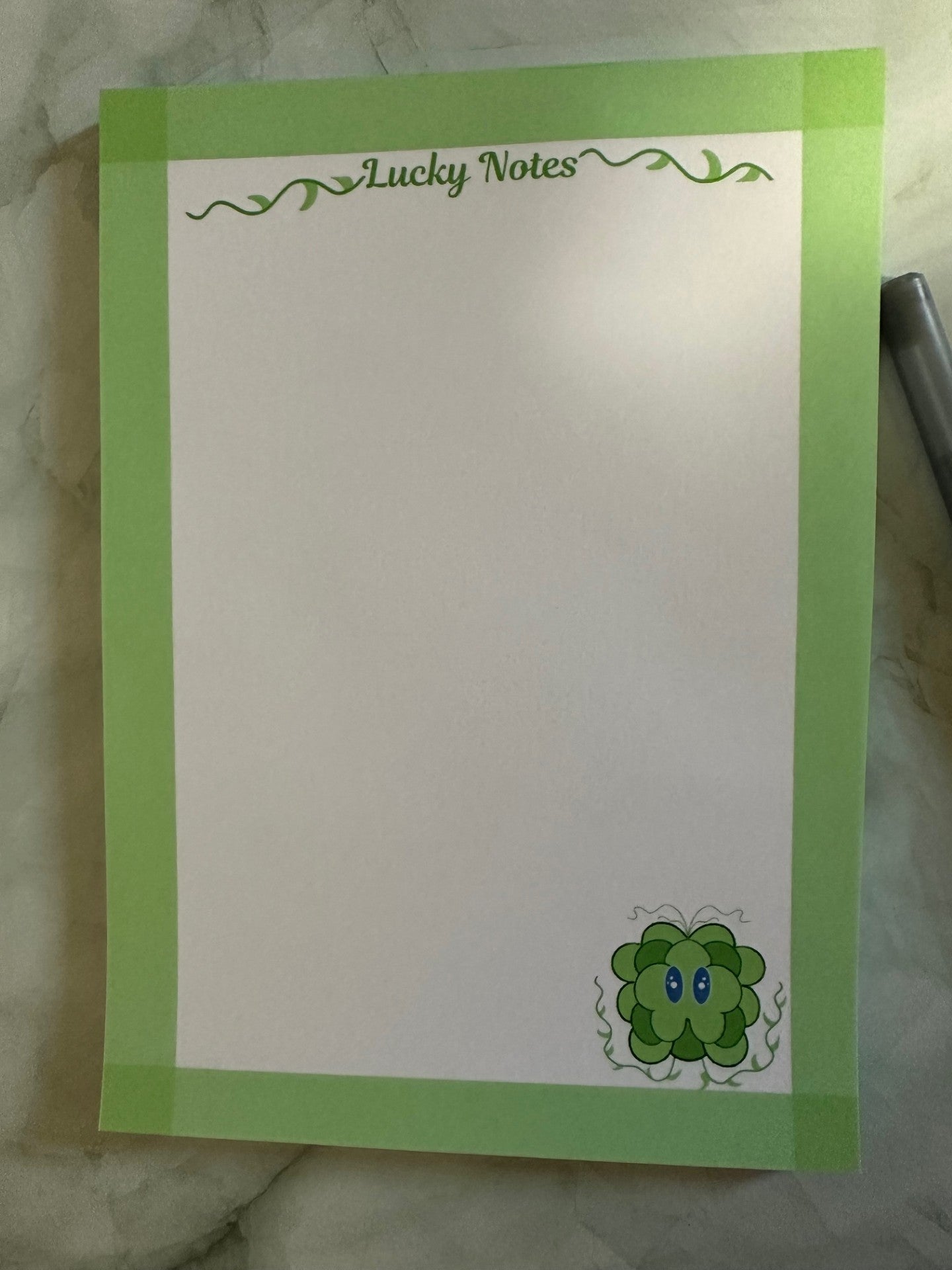 Note pad stating "lucky notes" on top. With fictional character lucky displayed on the bottom right. Lucky is a green and dark green color with his vines up.