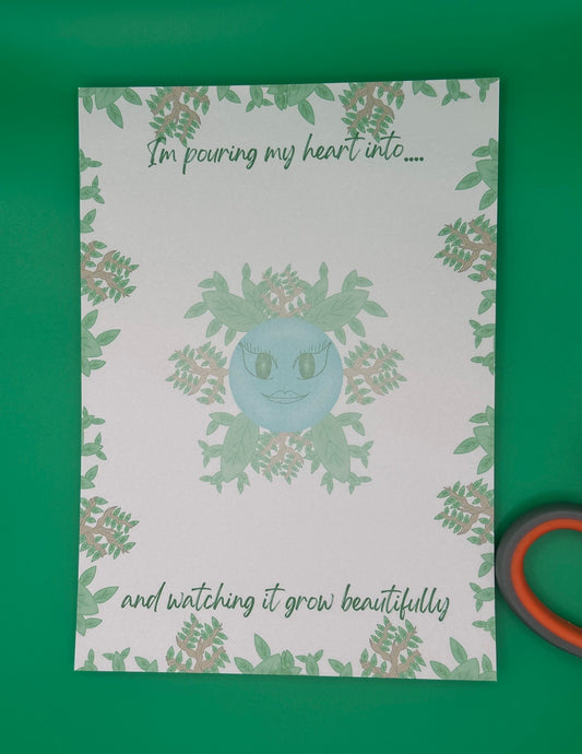 A notepad that has blue character with green eyes and lips. The character has leaves and branches coming out of it. The notepad has leaves and branches all around the edges. The notepad has a heading on top that states "I'm pouring my heart into...." and at the bottom states" and watching it grow beautifully". The notepad is sitting on top of a green background with scissors .
