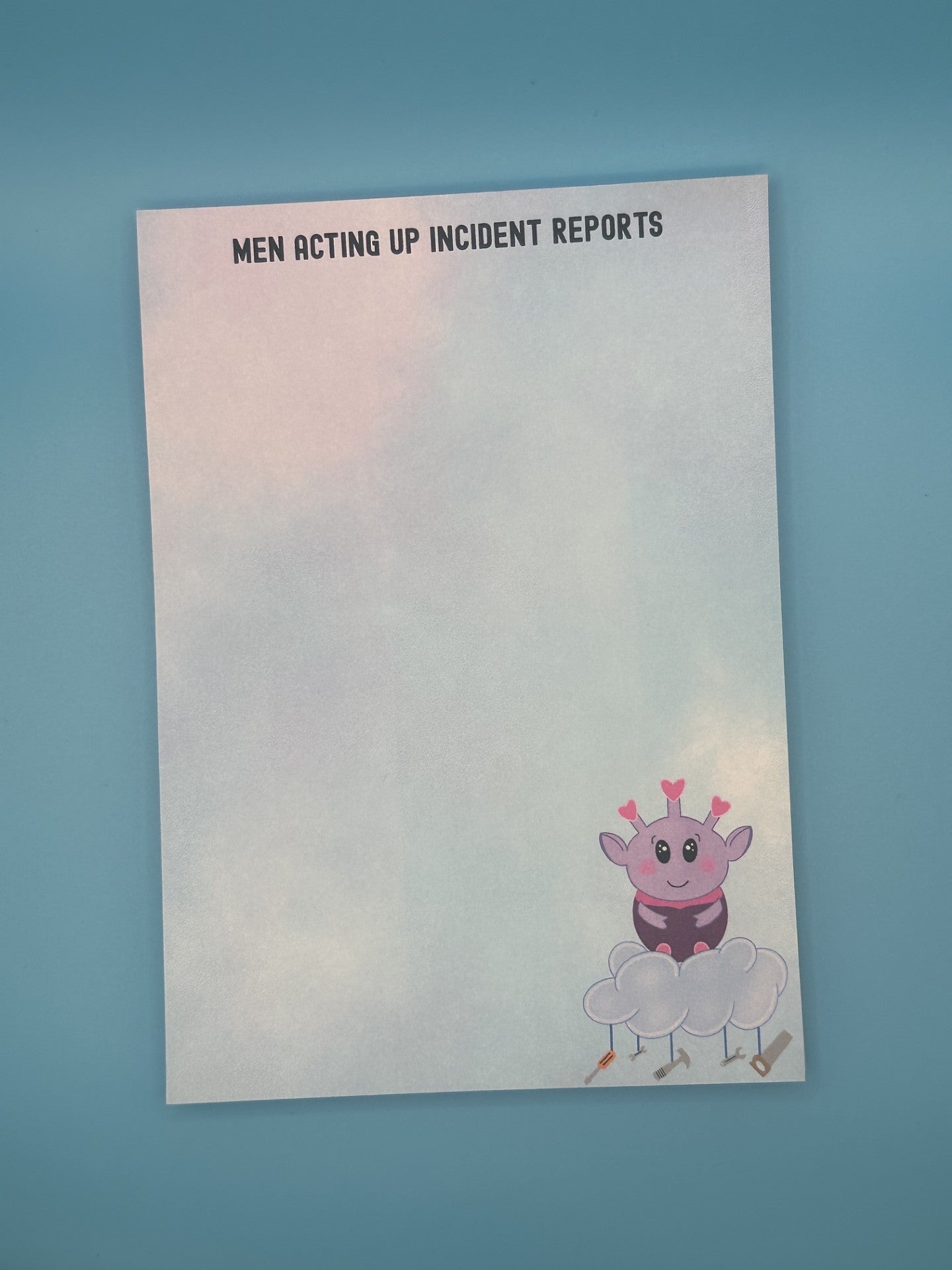 Notepad with a cartoon character at the bottom right of the notepad. The character looks like an alien who is purple and is sitting on top of a cloud with tools hanging from it. The notepad has a pastel-colored background, and on top of the notepad states 'Men Acting Up Incident Reports'. The notepad is sitting on a blue background.