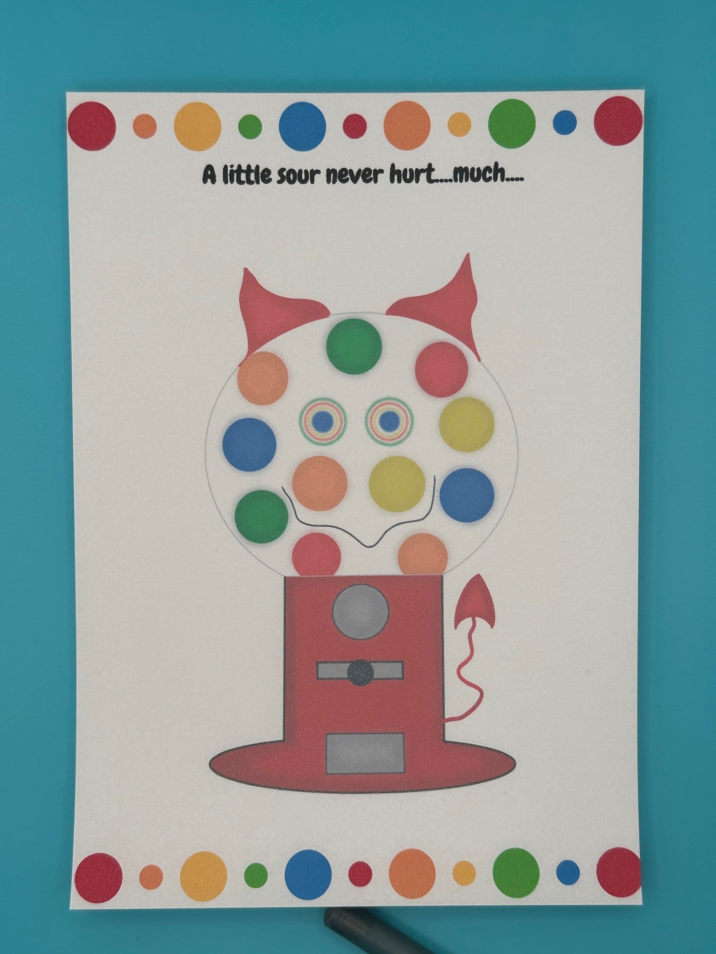A notepad that has a red gumball machine character. Inside of the gumball machine is different color gumballs and coming out of the character is red horns and a red devil tail. The notepad has red, orange, green and blue dots on the top of the notepad and bottom. The heading of the notepad states "A little sour never hurt....much...". The notepad is sitting on top of a blue background with a pen.