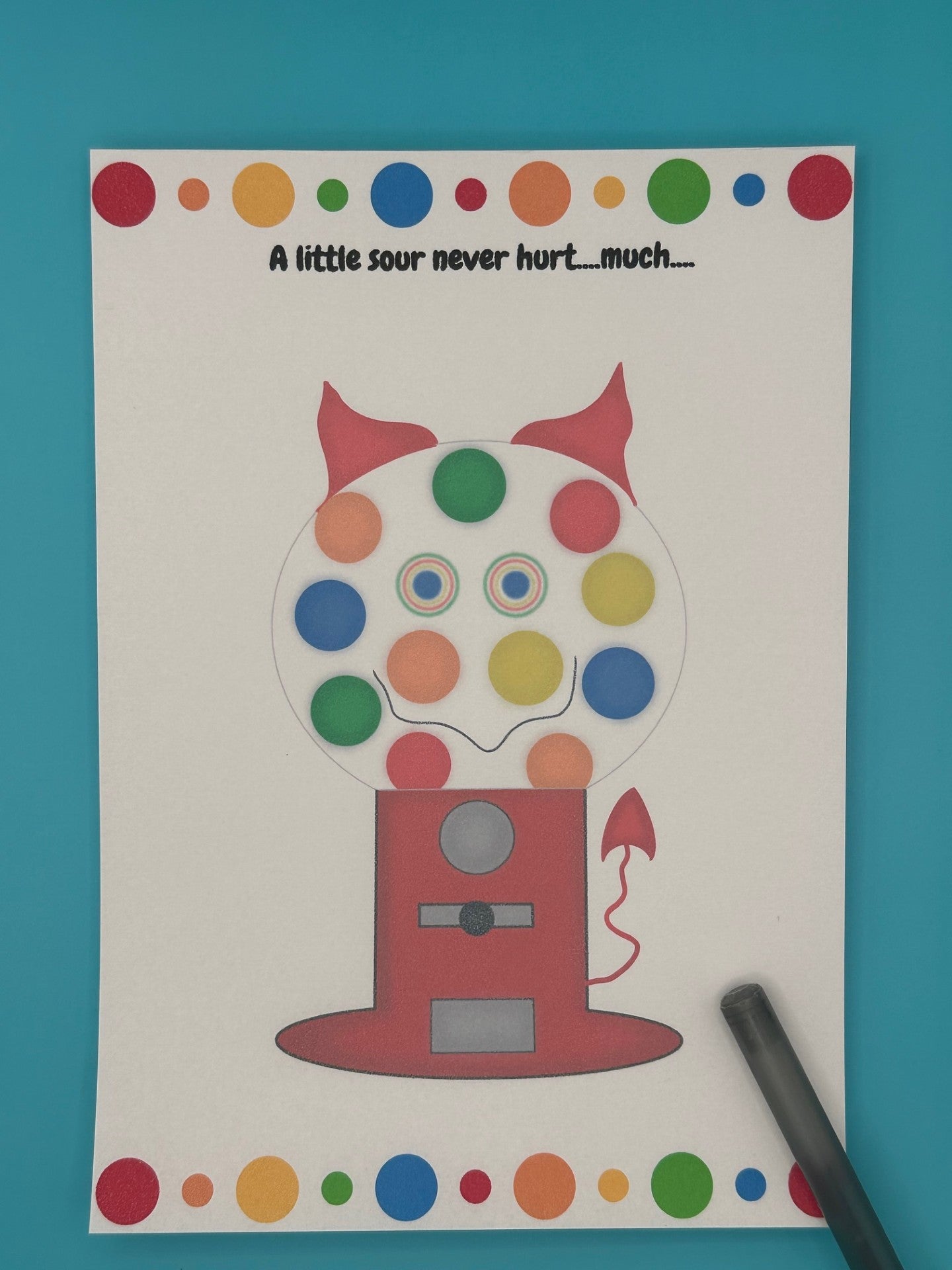 A notepad that has a red gumball machine character. Inside of the gumball machine is different color gumballs and coming out of the character is red horns and a red devil tail. The notepad has red, orange, green and blue dots on the top of the notepad and bottom. The heading of the notepad states "A little sour never hurt....much...". The notepad is sitting on top of a blue background with a pen.