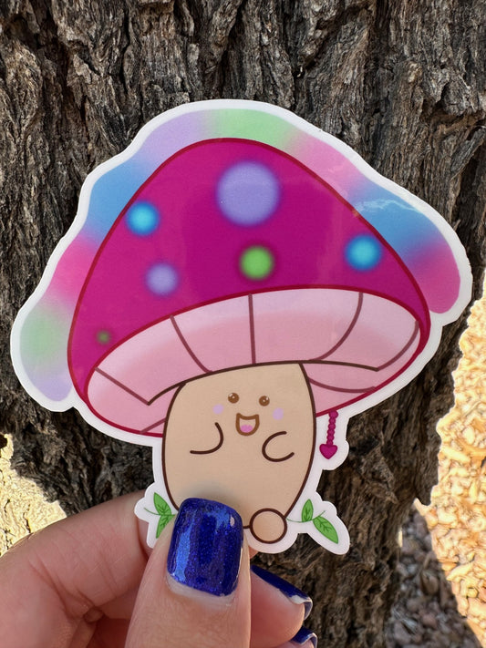 Hand-drawn Glimmer Bloom Beam mushroom sticker with vibrant colorful spots and green leaves at the base, held against a real tree trunk in natural light.