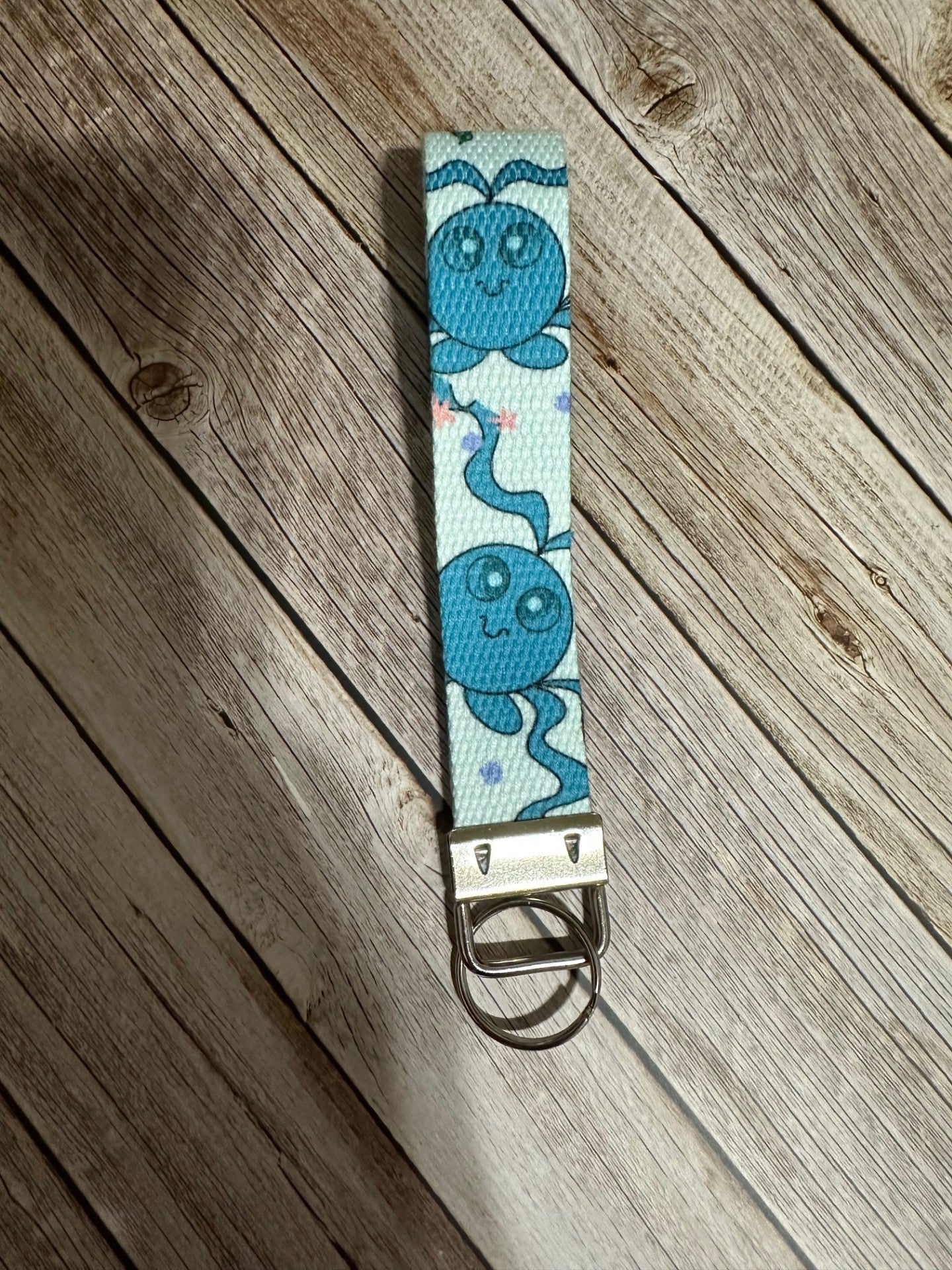 Front view of the keychain wristlet with a blue-colored fictional cartoon character on a wooden surface.