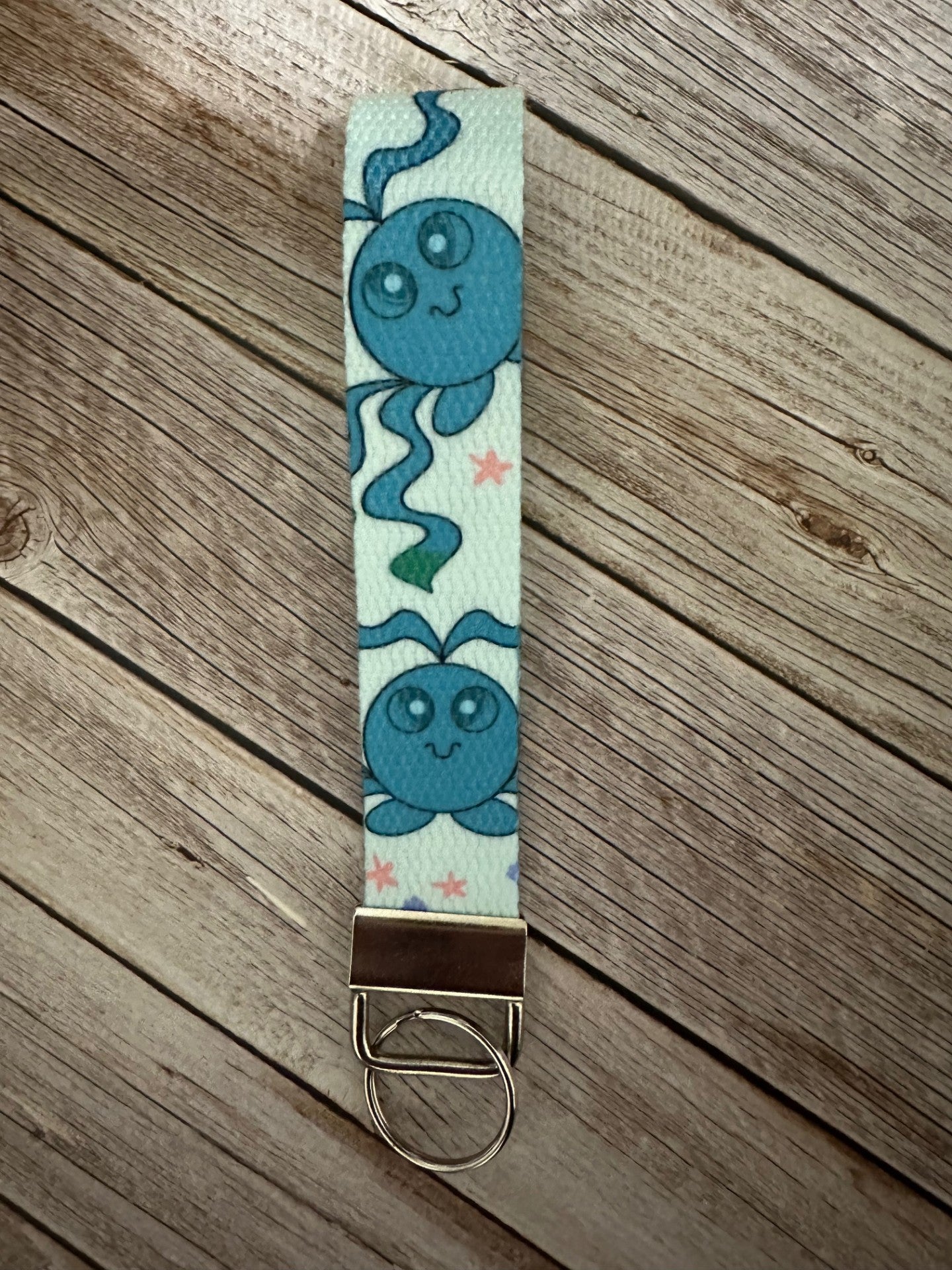 Keychain wristlet with a blue-colored fictional cartoon character on a wooden surface.