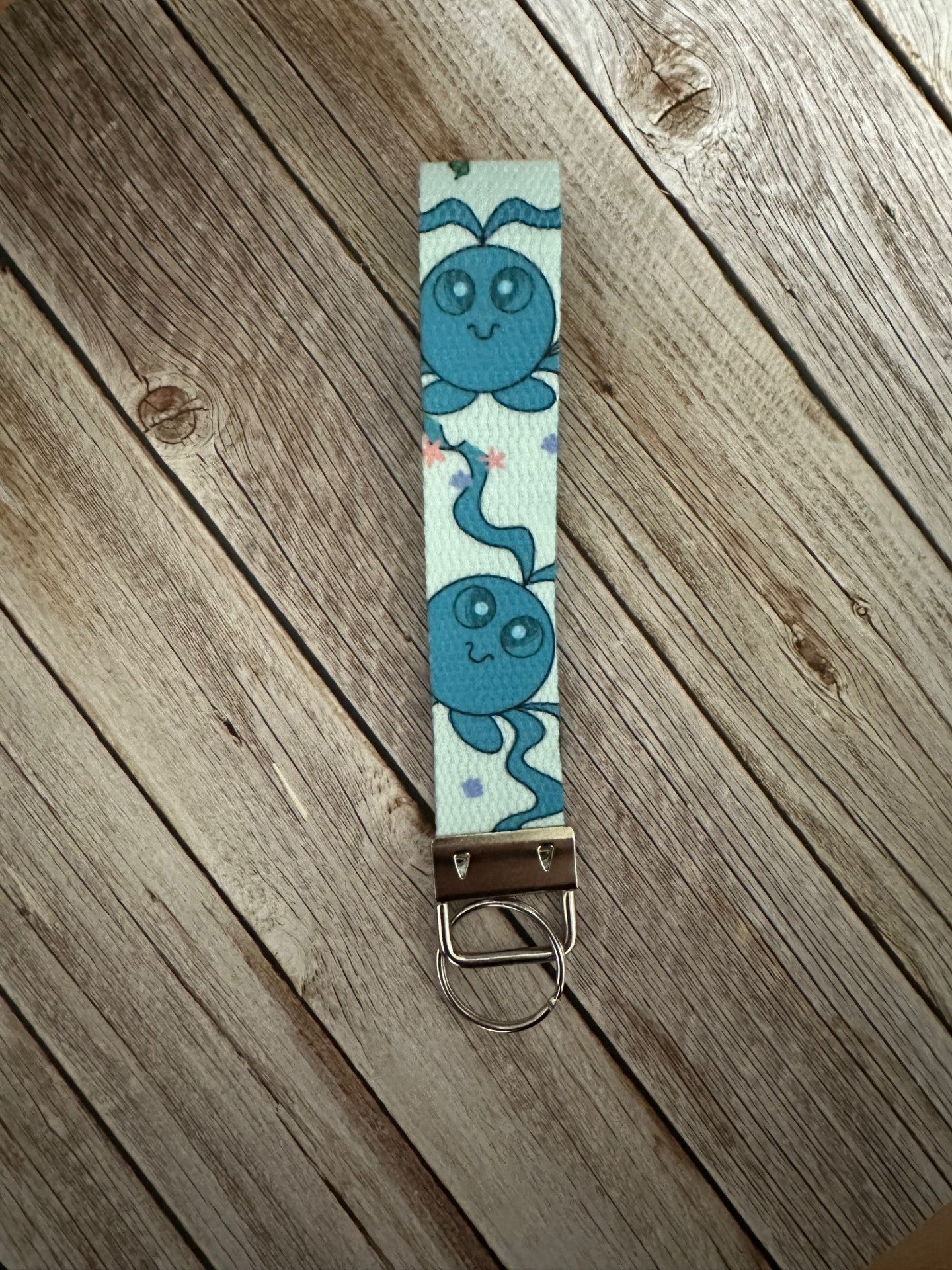 Keychain wristlet with a blue-colored fictional cartoon character on a wooden surface.