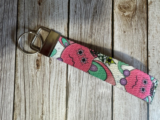 Wristlet with a pink flower pot illustrated design that has yellow flowers coming out of it, sitting on a wooden surface. 