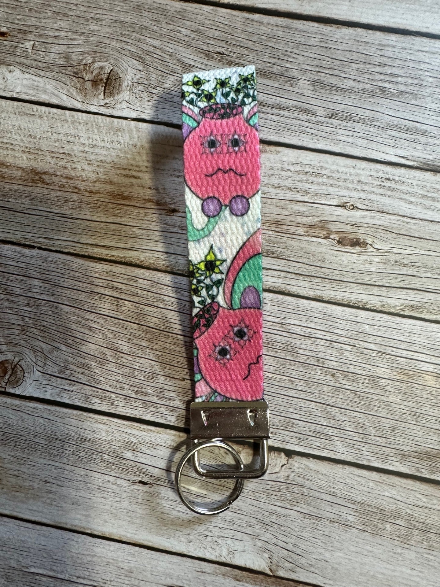 Wristlet with a pink flower pot illustrated design that has yellow flowers coming out of it, sitting on a wooden surface. 