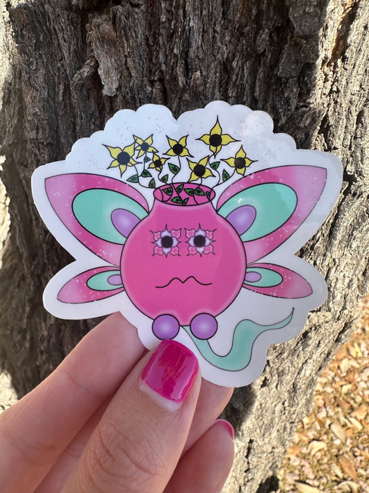 Colorful pastel pink, purple, and turquoise sticker of a fairy pot character with butterfly wings and flowers coming out of it held against a tree trunk.