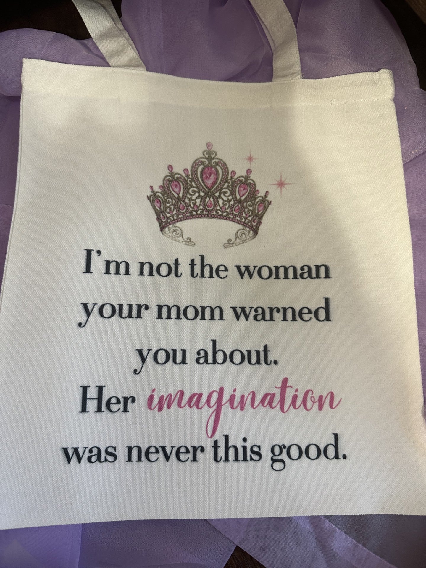 White tote bag featuring a pink and silver crown graphic and the quote: 'I'm not the woman your mom warned you about. Her imagination was never this good.