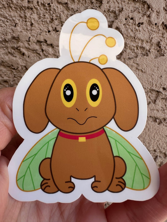 Cartoon brown dog that has big yellow and black eyes with green butterfly wings held against a textured beige background.