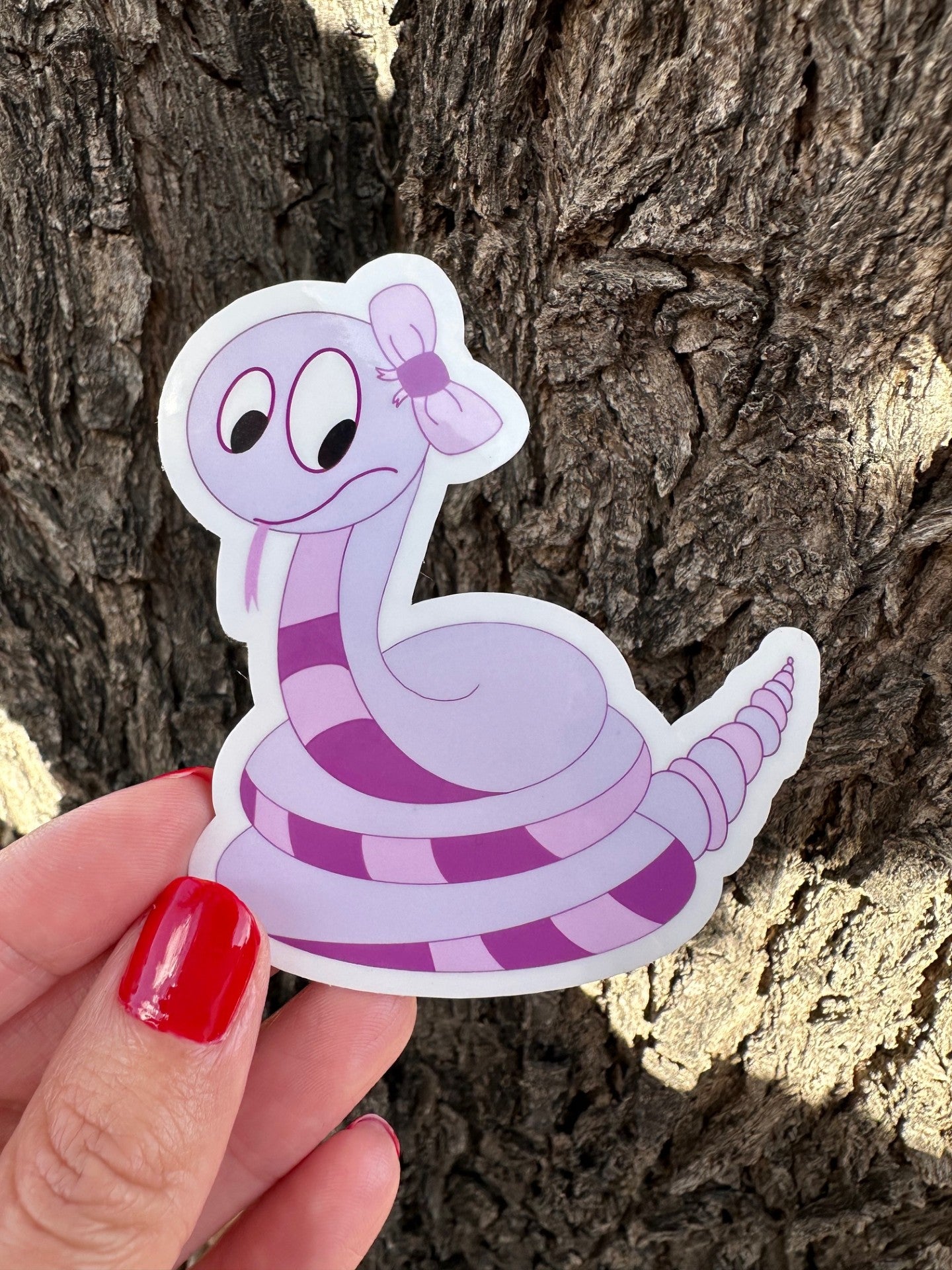 Cartoon non-fiction character snake shape with a purple color sticker held against a tree bark background.