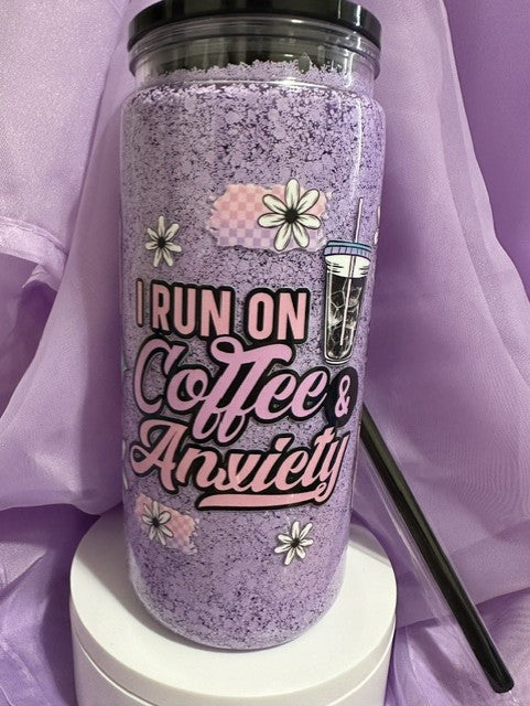 A purple snow globe tumbler with a black lid and straw, featuring the text: 'I RUN ON Coffee & Anxiety,' along with daisy and iced coffee illustrations.