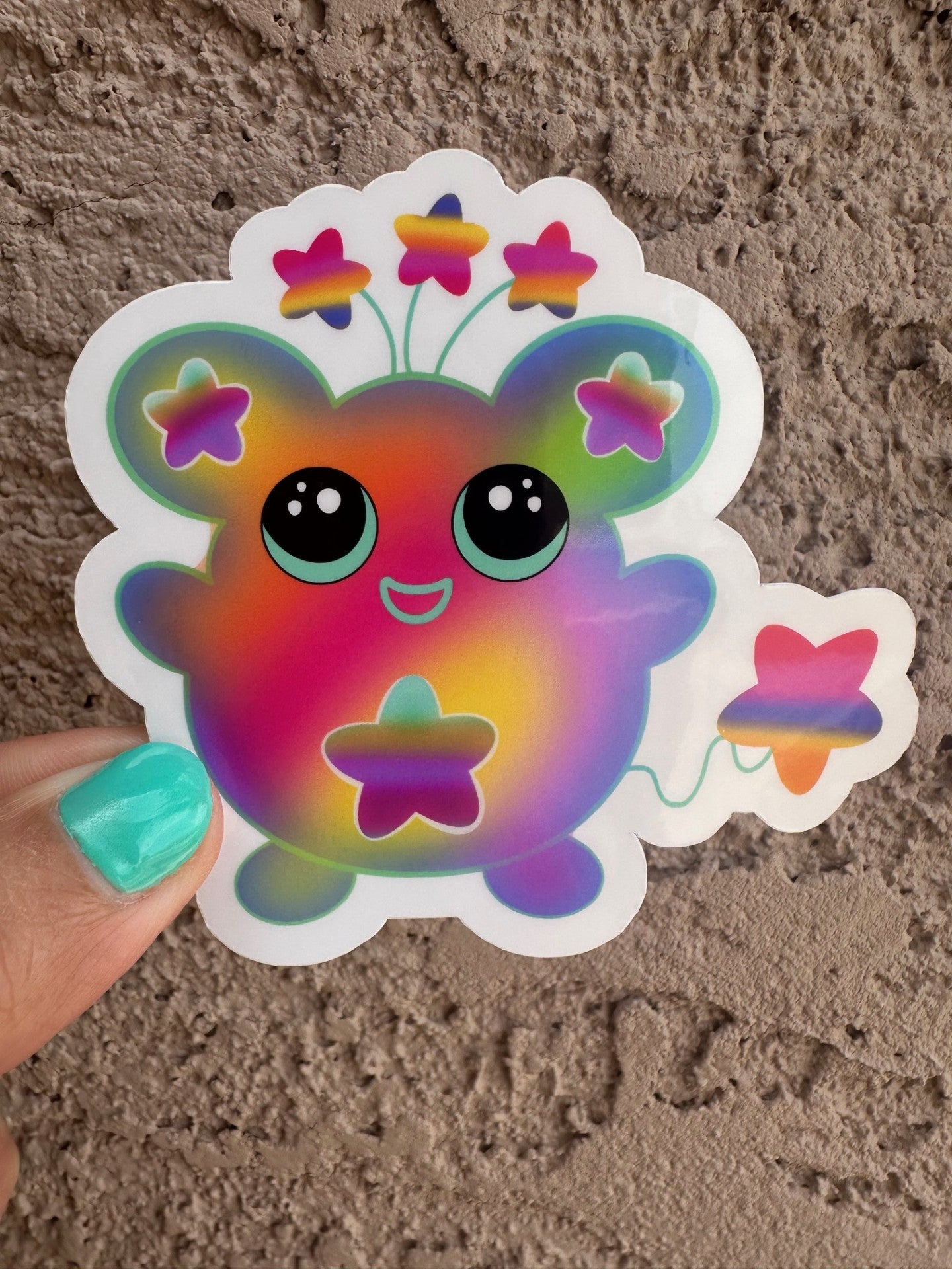Colorful cartoon character sticker that has stars on the ears and a star on the stomach. The character has different colors like pink, purple, green, and yellow. The character has stars coming from outside of its head and has a star as a tail. 