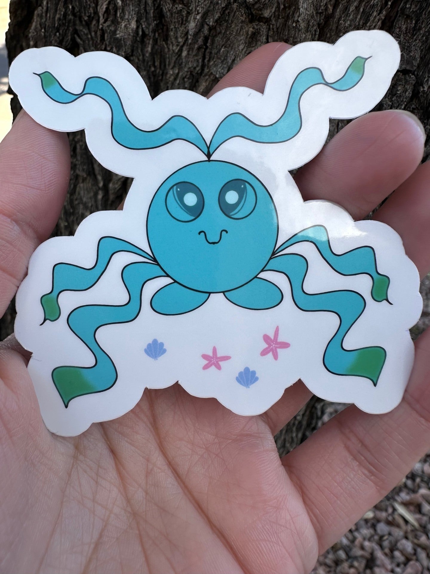 A sticker featuring a blue octopus sea like creature with long, wavy tentacles that have green tips, along with small illustrations of pink starfish and blue seashells.