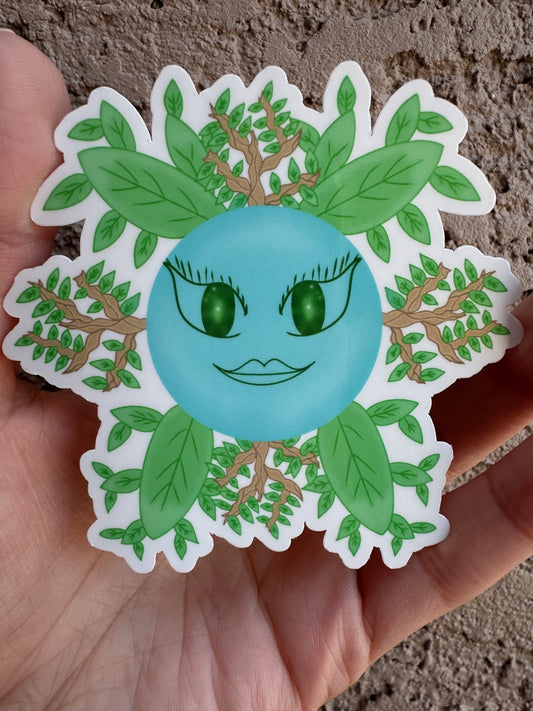 Glossy sticker of a fictional character shaped like a blue circle with green eyes and a green mouth, coming out of which are green leaves and branches. 