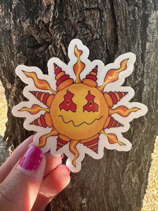Hand holding a sun-shaped sticker with a face against a tree bark background.