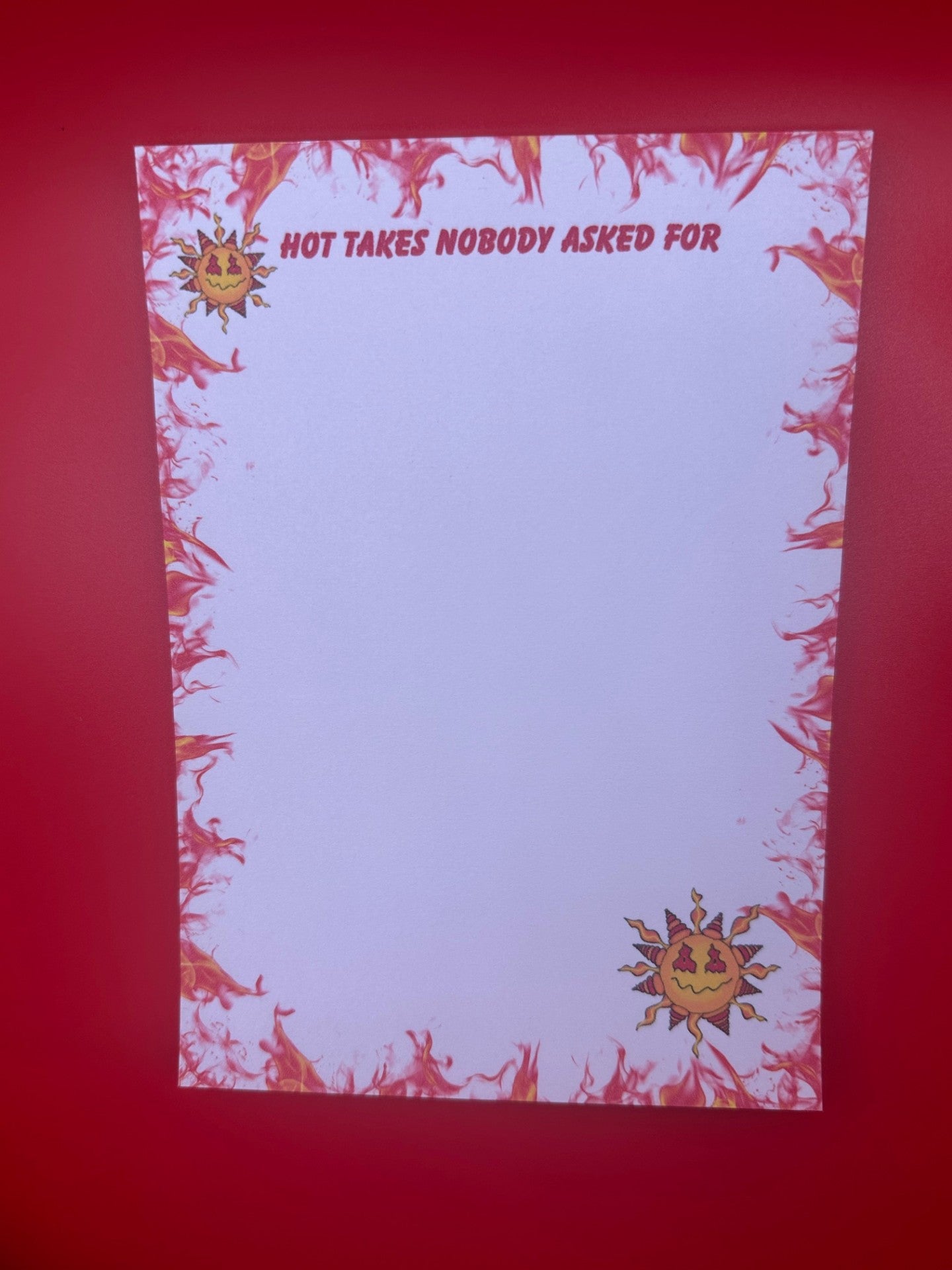 A notepad with character on top and bottom of notepad that looks like a sun with yellow and red colors and a smirk face. The notepad edges all around the corners have orange and red flames with the notepad heading of "Hot takes nobody asked for". The notepad is sitting on a red background.