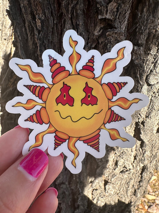 Sun-shaped sticker with a face held against a tree trunk.