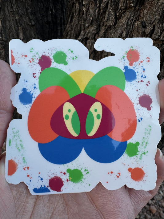 A sticker featuring an abstract, colorful creature made of layered organic shapes in orange, green, yellow, blue, red, and purple, surrounded by multi-colored paint splatters.